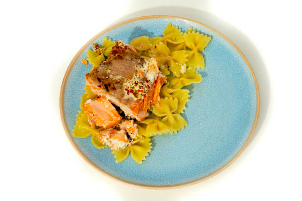 A vibrant plate showcases a generous serving of tender salmon alongside bright green bowtie pasta, garnished with spices for added flavor.