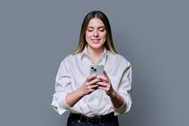 istock Young beautiful woman looking at smartphone on grey studio background 2197246142
