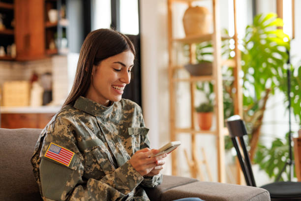istock Smiling United States Army Soldier Relaxing on Sofa Using Smartphone 2197254197