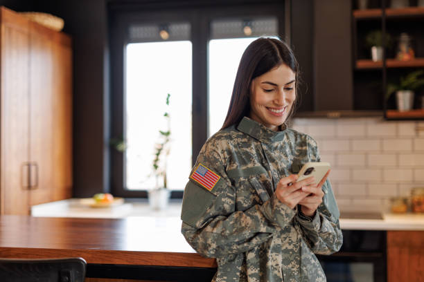 istock Smiling US Army soldier woman using mobile phone at home 2197254239