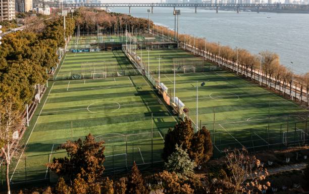 Aerial view of soccer fields by a river with a bridge in the background, showcasing a blend of nature and urban landscape.