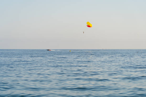 Parasailing in the open sea: a bright parachute pulls a boat, a person enjoys flying over the waves on a sunny day.