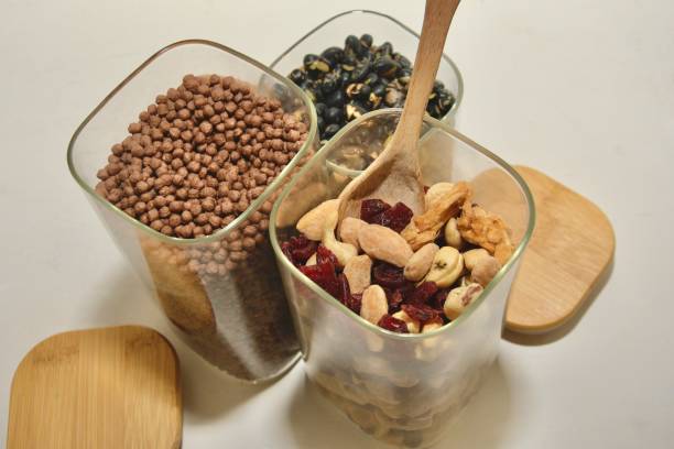 A three-quarter view of three open glass superfood dispensers, with the spoon now placed inside the dried fruit container, emphasizing a zero-waste, eco-friendly lifestyle.