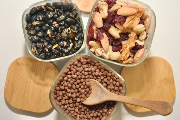 A top-down perspective of three open glass dispensers full of healthy superfoods, with a wooden spoon resting inside the jar filled with cereal.
