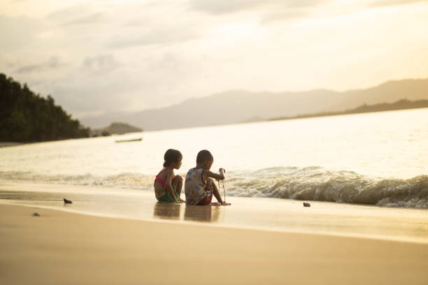 Two children enjoying a sunny day at the beach, splashing each other in the shallow waves while the sun sets, creating a warm, golden atmosphere around them.