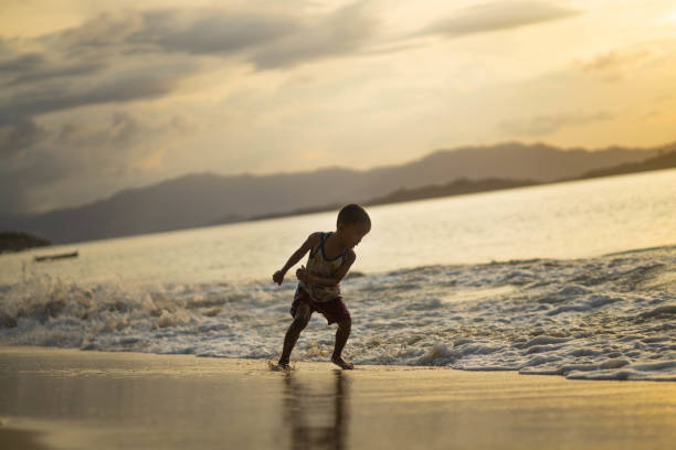 A young boy joyfully interacts with the waves at dusk, embodying the pure joy of childhood moments spent in the enchanting embrace of the sea.