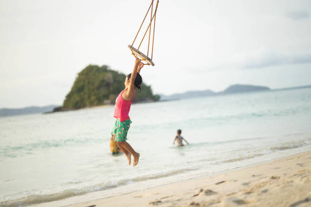 A child joyfully swings into the air over the sparkling waters at sunset, encapsulating the carefree spirit and beauty of joyous outdoor playtime during summer.