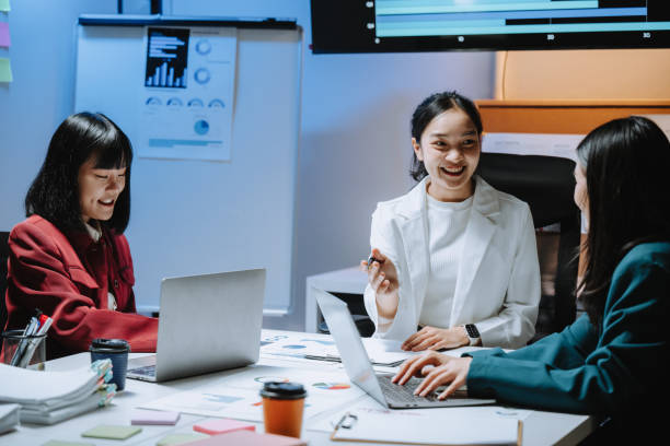 istock Three young asian businesswomen are discussing a new project in a modern office, using laptops and analyzing charts and graphs displayed on a whiteboard and a screen 2197260774