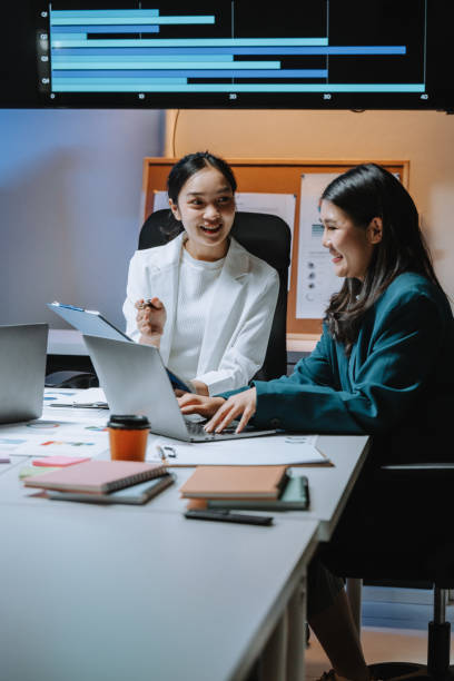 istock Two young asian businesswomen are smiling and collaborating on a project, analyzing charts and data on a laptop in a brightly lit office meeting room 2197260794