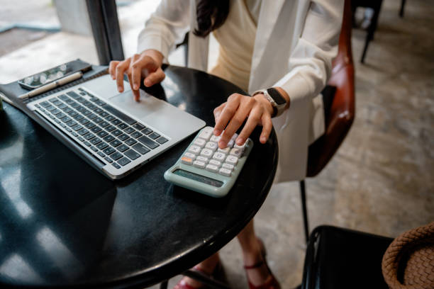 istock Businesswoman sitting at a cafe table, focused on managing finances while using a calculator and laptop, enhancing productivity in a modern, casual workspace 2197262849