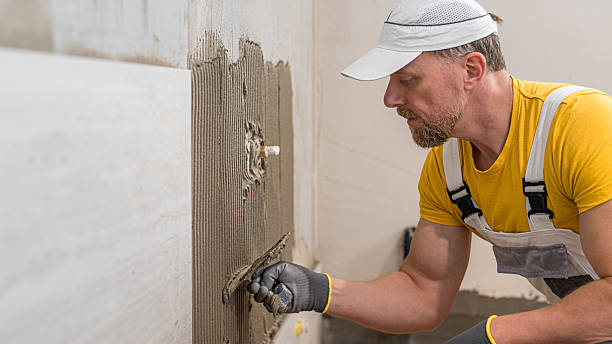 istock Tiling with large format tiles. A tiler uses a notched trowel to spread tile adhesive onto a wall. 2197263965