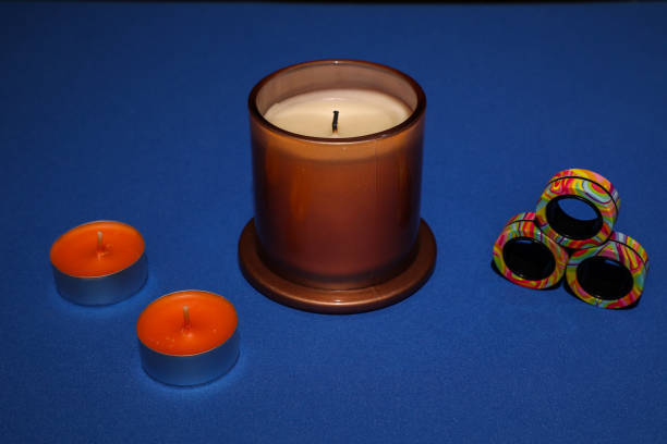 One large candle and two small candles stand on a blue textured surface, next to them are three round colored magnets.