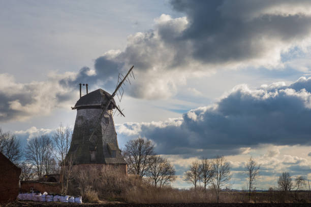 A horizontal color photo depicting an old windmill against a background of beautiful clouds