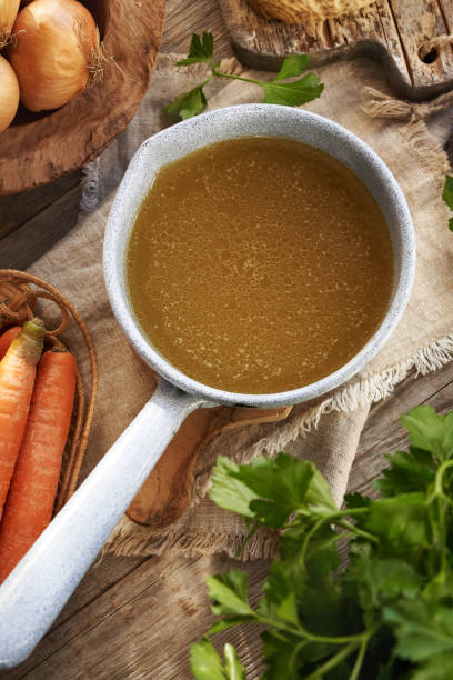 istock Chicken bone broth in a blue pot on a table with fresh vegetables 2197271574
