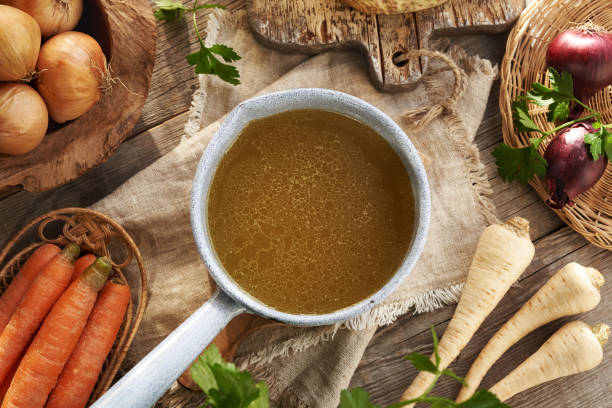 istock Chicken bone broth or soup in a pot and fresh vegetables on a wooden table 2197271575