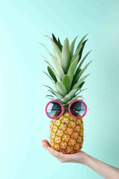 istock Female hand holding ripe pineapple with sunglasses on mint background 2197276868