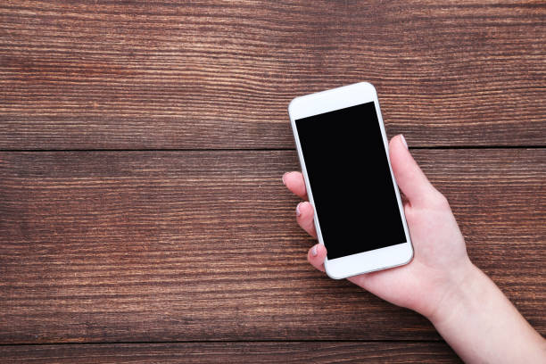 istock Female hand holding smartphone on wooden background 2197281742