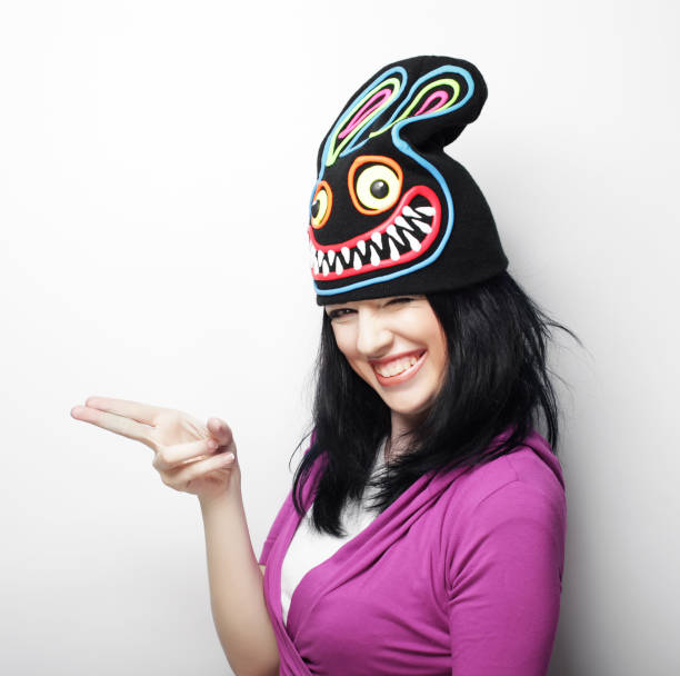 Playful young woman in funny hat with rabbit, studio shot
