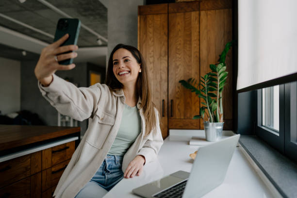istock Young woman taking a selfie in her modern kitchen using a smartphone 2197296487