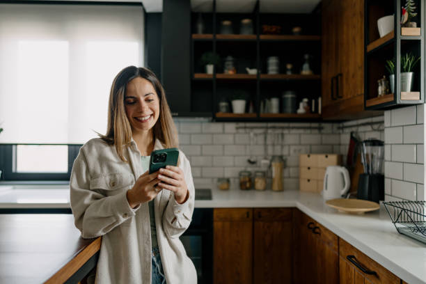 istock Young Woman Smiling and Using Smartphone in Modern Kitchen 2197296539