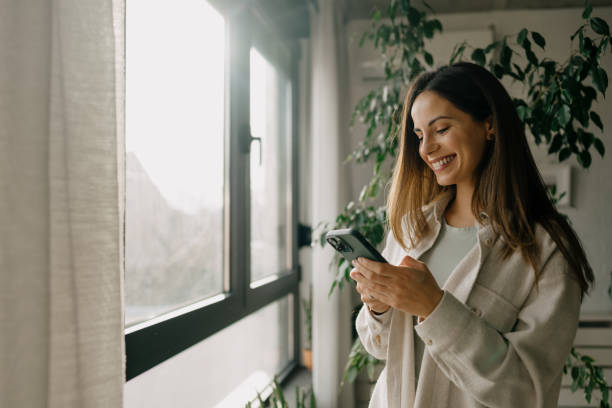 istock Young woman using smartphone near window at home 2197296562