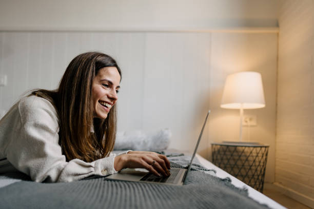 istock Young Woman Lying on Bed and Typing on Laptop 2197296618