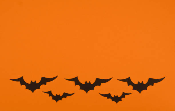 Black bats flying across an orange backdrop, creating a Halloween atmosphere in autumn