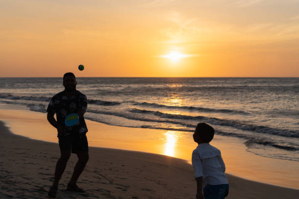 Father and son enjoying a game of beach tennis during a vibrant sunset at the beach