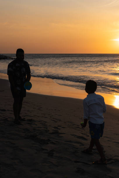 Father and son are enjoying a beautiful sunset on the beach while playing catch