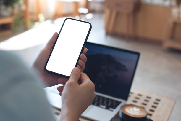 istock Cell phone white screen mockup, Woman hand holding mobile phone with blank screen while working at coffee shop. Business woman using smartphone, mockup for display mobile app interface design 2197321924