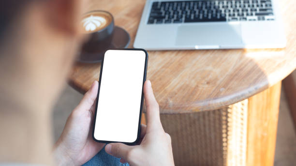 istock Cell phone white screen mockup, Woman hand holding mobile phone with blank screen while working at coffee shop. Business woman using smartphone, mockup for social media advertisement 2197326312