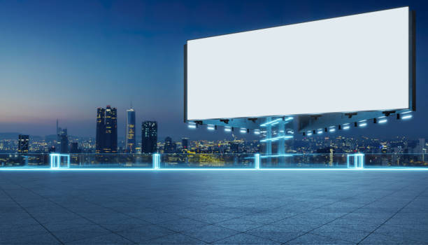 Empty billboard glowing on modern rooftop with illuminated city skyline view at dusk