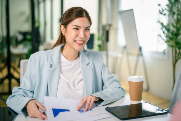 istock A smiling woman sits at a table with documents and a coffee cup, engaged in a discussion in a bright office environment. Professional Business Team Meeting to Analyze Financial Reports 2197335199