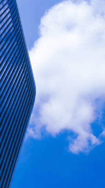 A sleek, modern skyscraper with soft, curving lines contrasts against a vivid blue sky adorned with fluffy white clouds, showcasing an interplay of architectural precision and natural serenity.