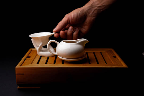 A beautifully captured moment of a traditional Chinese Gongfu tea ceremony. A hand gracefully pours tea from a delicate teapot onto a tea pet, surrounded by an elegant tea set on a wooden tray. The dark background enhances the aesthetic and cultural significance of this mindful tea ritual