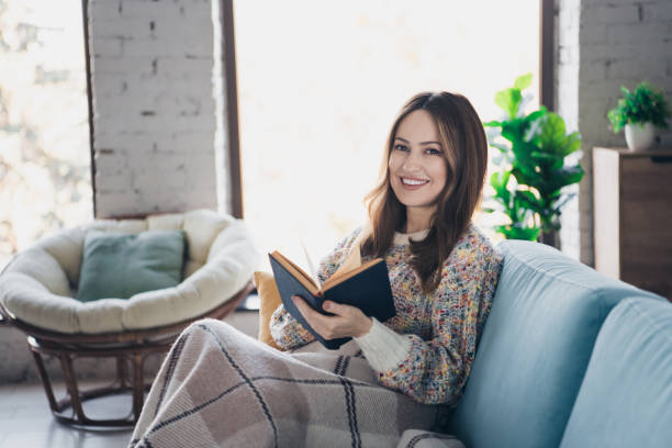 istock Young woman reading book at home cozy interior during a relaxing day 2197355511