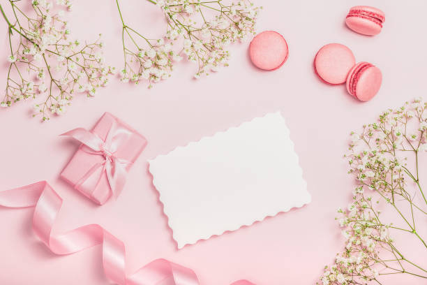 istock Flat lay composition with empty blank, macaroon, gift box, satin ribbon and gypsophila on pink background. Stylish women's workplace. Greeting card 2197356622