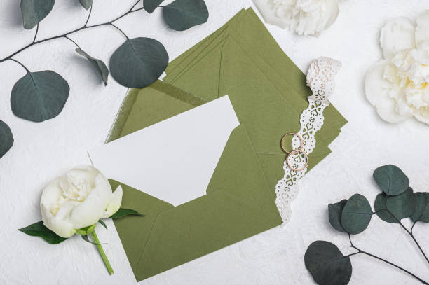 istock Wedding invitation or greeting card mockup with green envelopes, white peony flowers and openwork ribbon on light background. 2197356765