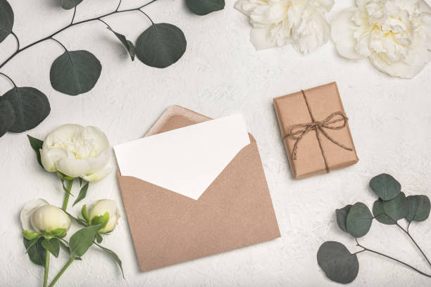 istock Greeting card mockup with craft envelope, gift box and white peony flowers and eucalyptus sprigs on light background.. 2197356798