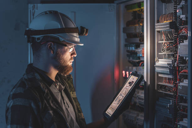istock Electrician in overalls, focused on work in switchboard with fuses, using tablet. 2197357364