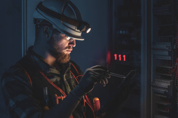 istock Electrician in overalls, focused on work in switchboard with fuses, using tablet. 2197357396