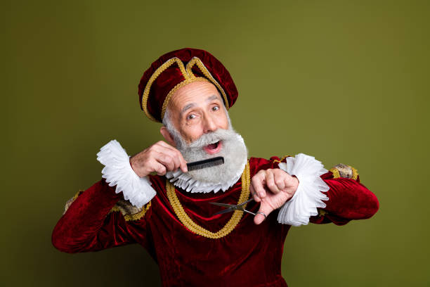 istock Elderly Man in Renaissance Costume Holding Comb and Scissors on Khaki Background 2197358812