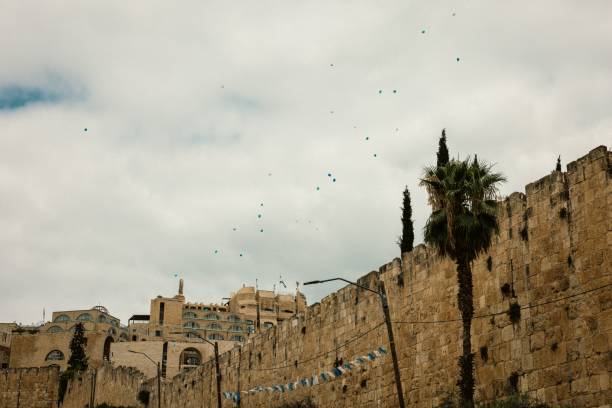 Historic stone walls in Jerusalem with floating blue balloons against a cloudy sky, capturing a serene urban scene.