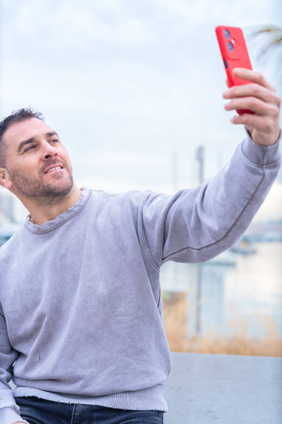 istock Smiling Man Taking a Selfie with Red Smartphone Outdoors.Vertical 2197369502