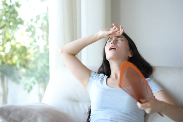 Stressed asian woman fanning suffering heat stroke at home stock photo