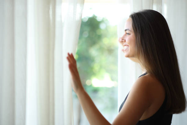 istock Young woman looking through a window at home 2197370927