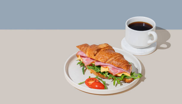 istock Croissant sandwich with ham, cheese, tomato  and arugula on a plate on a light background 2197372542