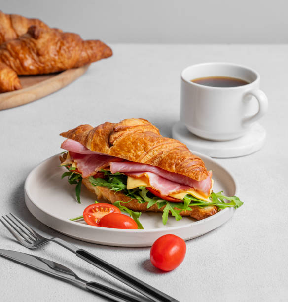 istock Croissant sandwich with ham, cheese, tomato  and arugula on a plate on a light background 2197372563
