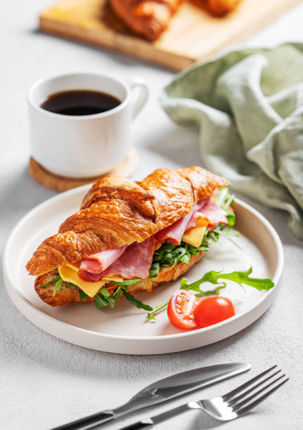 istock Croissant sandwich with ham, cheese, tomato  and arugula on a plate on a white background 2197372582