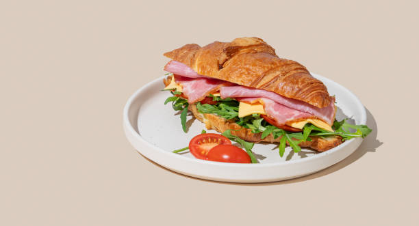 istock Croissant sandwich with ham, cheese and arugula on a plate on a yellow background with a shadow. 2197373065